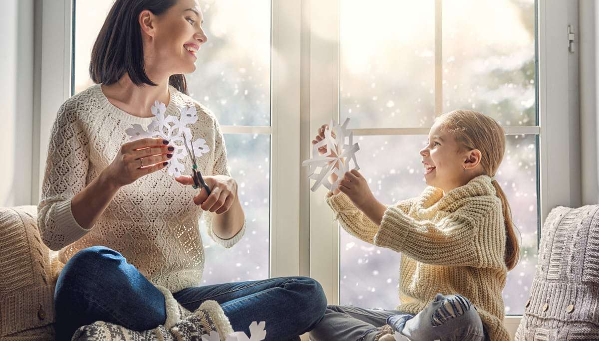 Мама с дочкой вырезают снежинки на окне